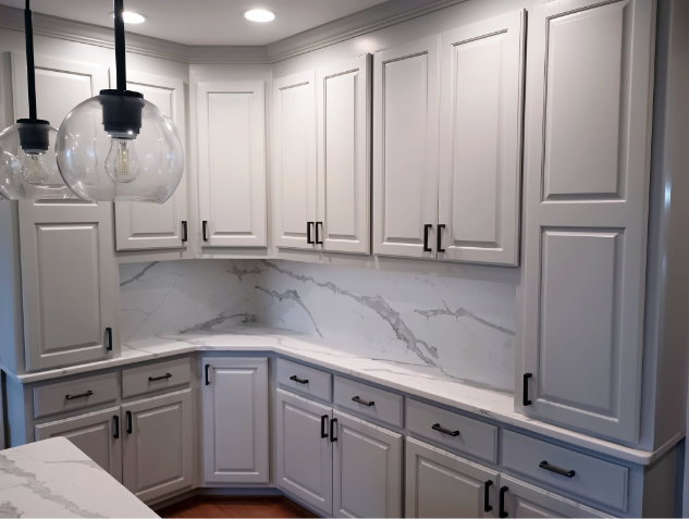 A modern kitchen with white cabinets, marble countertops, and globe pendant lights hanging over an island counter